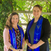 Revs. Christina (left) and Hannah, wearing blue stoles, and standing under an arbor